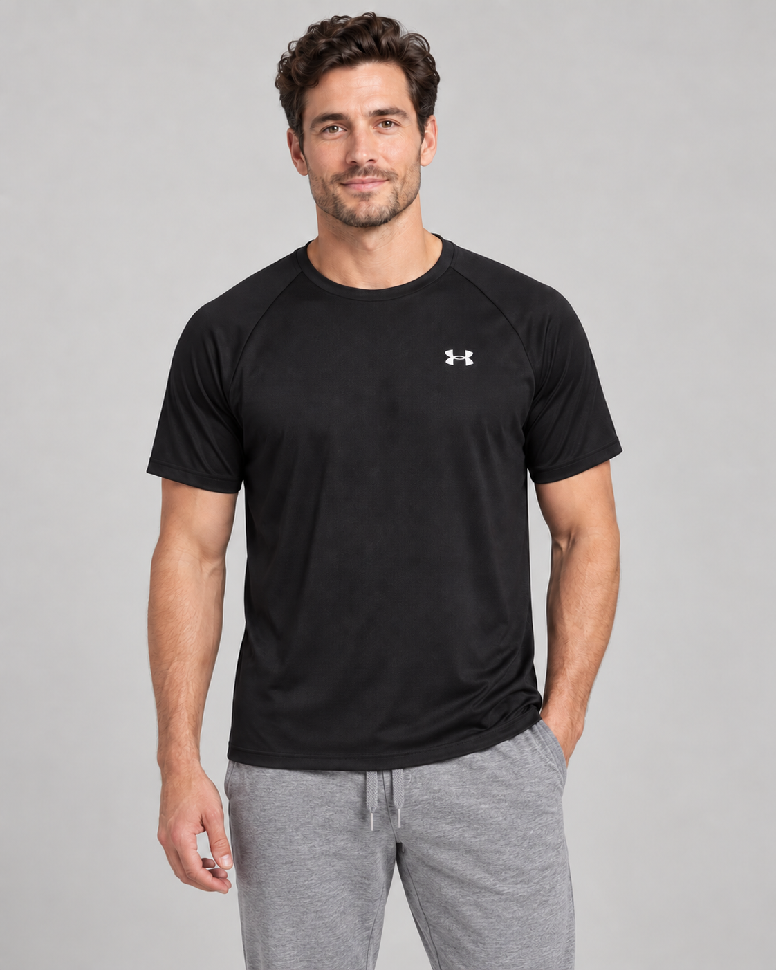 Male model wearing a black Under Armour Tech Tee with white chest logo and grey joggers in a studio
